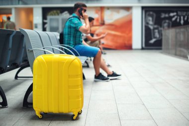 Modern yellow suitcase near chairs in waiting room. Waiting for flight or train. Travel abroad. Business trip.