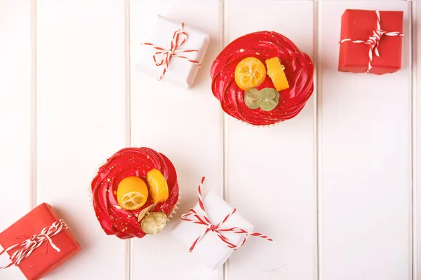 Tasty festive cupcakes and small christmas gifts on wooden background, top view. Christmas holidays — Stockfoto
