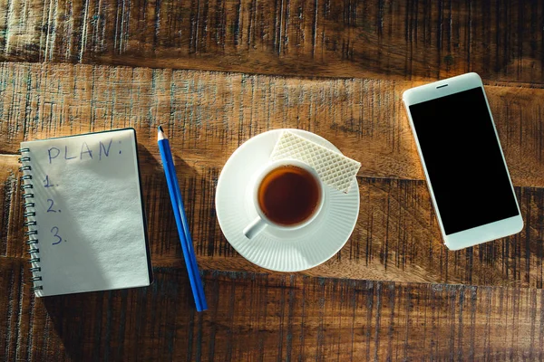 Café de la mañana con cuaderno y plan de acción en escritorio de madera, vista superior. Taza de café o té para el estado de ánimo . — Foto de Stock