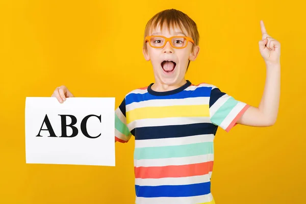 Izgatott, boldog kisfiú, aki leveleket tanul. A fiú sárga alapon tartja az Abc kártyát. Beszédterapeuta leckék. — Stock Fotó