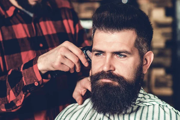 Jovem na barbearia. O barbeiro corta o cabelo do cliente. Um tipo barbudo bruto. conceito de serviço de cuidados com o cabelo . — Fotografia de Stock