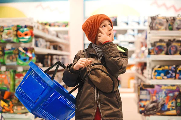 Boy choosing toy in big assortement in supermarket. It is difficult choice to buy a interesting toy. Little kid holding shopping cart in kids store — 스톡 사진