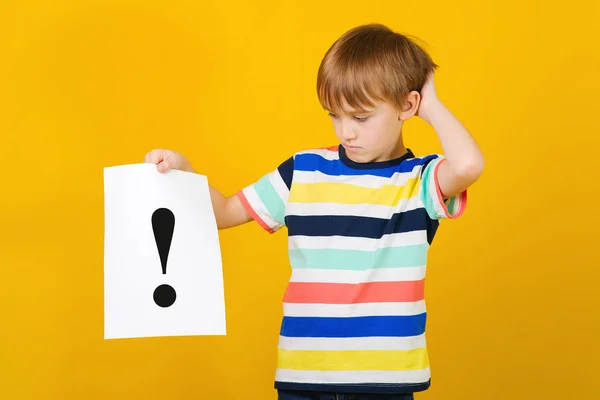 , denkt ein Junge. smart kid hält Papierbogen mit Ausrufezeichen. Nachdenkliches Kind auf gelbem Hintergrund — Stockfoto