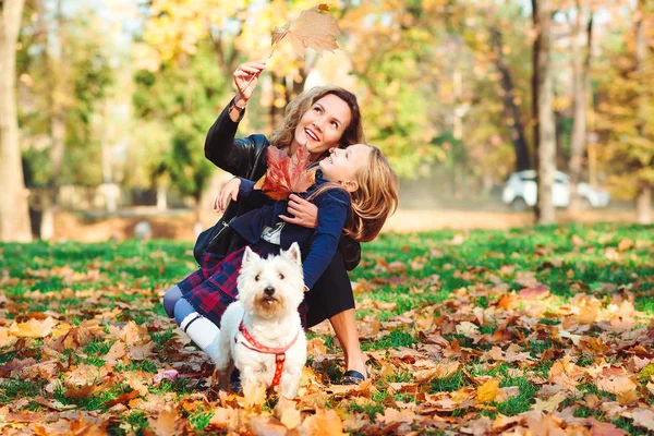 Família feliz com cão se divertindo no parque de outono. Mãe e sua filha brincando com o cão ao ar livre. Família, animal de estimação, animal doméstico e conceito de estilo de vida — Fotografia de Stock