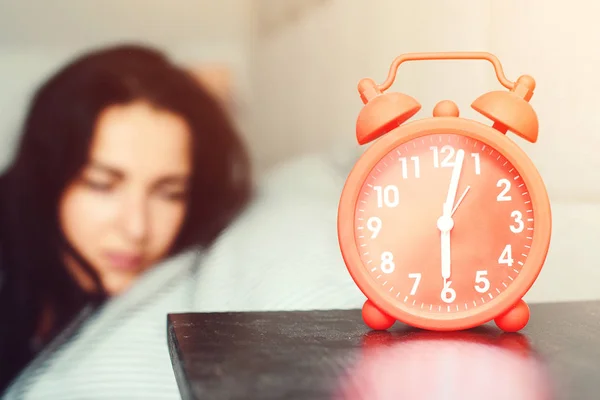 Reloj despertador en primer plano en el dormitorio en casa. Una joven durmiente en la cama. Despertar temprano por la mañana — Foto de Stock