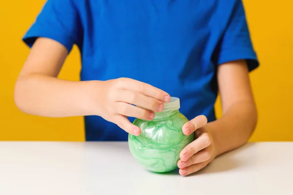 O rapazinho abriu o frasco com lodo. Brinquedo popular para criança. Criança bonito brinca com lodo verde — Fotografia de Stock
