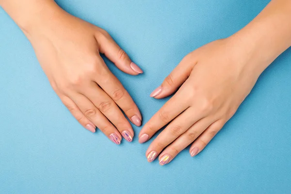Жіночі руки з ніжним манікюром на синьому фоні, вид зверху. Концепція догляду за шкірою — стокове фото