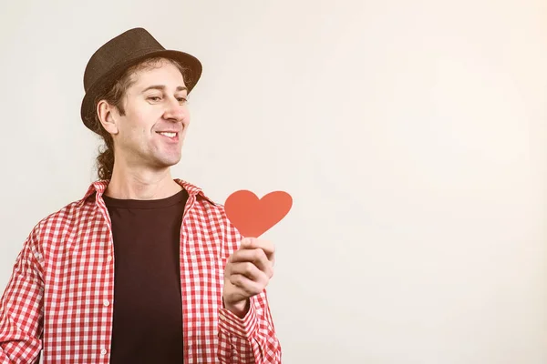 Funny guy wears retro hat and shirt. Guy holding red paper heart, prepares for Valentine day. Love, romantic feelings.