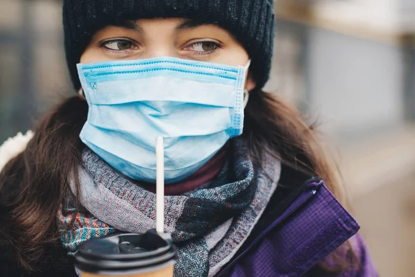 Frau in Schutzmaske geht mit Kaffee in Pappbecher durch die Stadt. Coronavirus-Epidemie in der Stadt. Person mit Mundschutz gegen übertragbare Infektionskrankheiten — Stockfoto
