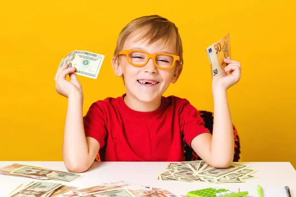 Happy smiling boy holding euro and dollar banknote. Excited little boy in glasses thinking where to invest money — Stok fotoğraf