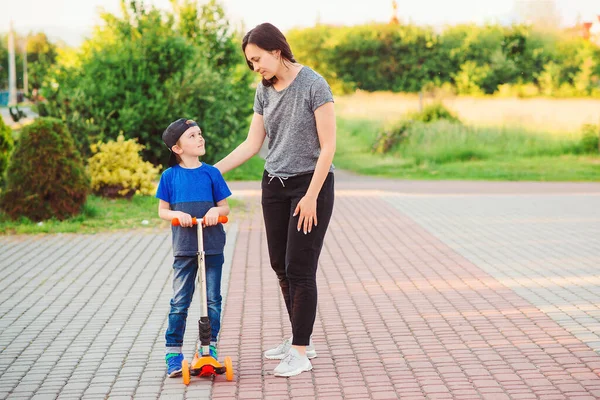 Mère réconfortant son fils après l'accident. . Garçon tombe pendant l'apprentissage du scooter. Sécurité, sport, loisirs avec les enfants . — Photo