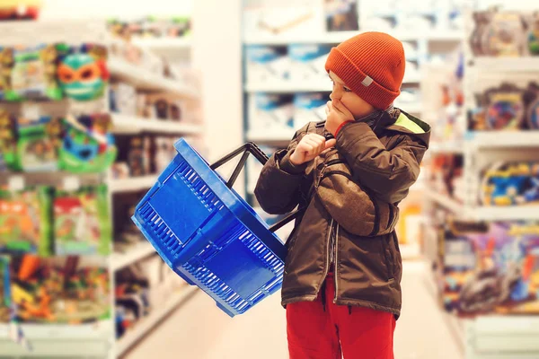 아이들 가게에서 쇼핑 카트를 들고 있는 아이입니다. 슈퍼마켓에서 큰 파티에서 장난감을 고르는 소년. 흥미 로운 장난감을 사는 것은 어려운 일이다 — 스톡 사진