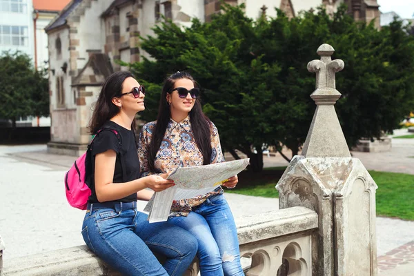 Girls searching for places on their map outdoors. Best girl friends traveling together in europe. Europe vacation, old city. Women in sunglasses. Beautiful girls looking for direction in the city.