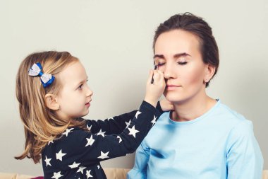 Kızı, annesinin makyajını yapıyor. Anne çocukla vakit geçiriyor. Sevgi dolu bir aile. Anne ve kızı evde birlikte eğleniyorlar. Anne ve kız anneler gününü kutluyor..