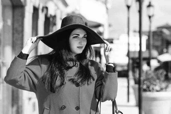 Confident woman wearing trendy black hat. Model posing in street of european city. Woman with long hair. Elegant woman walking in city. Shopping day, travel and lifestyle. Female fashion.