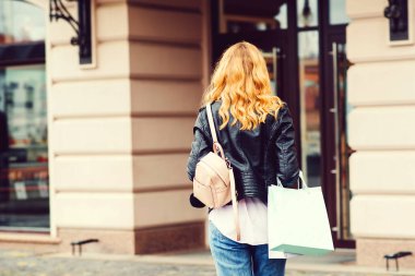 Alışveriş çantalı kadın, arka manzara. Kadın modası. Alışverişe giden çekici bir kız. Dışarıda elinde renkli çantalar tutan bir kadın. Moda alışverişçisi kadın. Alışveriş torbaları. Şehirde poşetlerle alışveriş koliği.