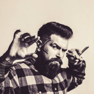 Şık sakallı adamın portresi. Berber elinde makas ve düz jilet tutuyor. Küçük işletme, berber dükkanı. Yakışıklı bir kuaför. Erkek tıraşı. Erkek sakalı, moda. Profesyonel berber aletleri.