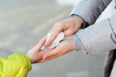 İnsanlar dışarıda antiseptik ıslak mendille ellerini dezenfekte ediyorlar. Mikrop bulaşmasını önlemek için antiseptik peçete, bakteri, koronavirüs, virüs. Anne ve çocuk ıslak mendille elleri dezenfekte ediyor..