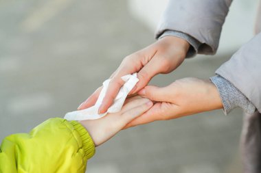 Kadın, çocuk ellerini antiseptik dokularla temizliyor. El hijyeni. Antibakteriyel ıslak mendil kullanan bir kadın. Mikrop, bakteri, koronavirüs ve virüsün yayılmasını önlemek için antiseptik peçete..