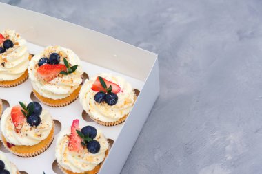 Çilekli ve yabanmersinli tatil kekleri. Kek ambalajı, gri arka planda teslimat kutusu. Şekerli hediye kutusu. Farklı lezzetli kekler. Meyveli keklerle dolu karton kutu..