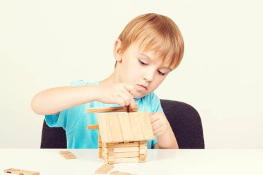 Çocuk evde tahta bloklarla oynuyor. Akıllı çocuk küçük bir ev inşa ediyor. Çocuk yeni bir rüya evi yapıyor. Çocuklar için yaratıcı bir eğlence. Bir şey yaratmak için tahta bloklar. Aile rüyası.