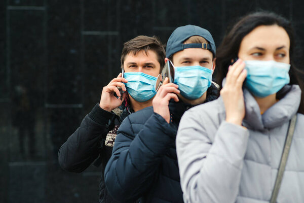 Group of young volunteers wearing face masks with mobile phones. Volunteers are ready to help. Call to volunteers. The concept of mutual assistance and support. World coronavirus pandemic.