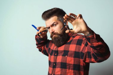 Sakallı yakışıklı berber elinde makas ve usturayla. Sakallı şık bir berber. Profesyonel berber aletleri. Klasik berber dükkanı, tıraş. İş için. Erkek tıraşı. Acımasız adam mavi üzerine izole edilmiş..