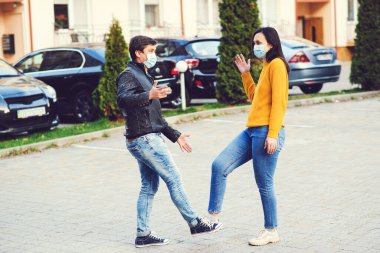 Genç çift ayaklarıyla selamlıyor. Kız ve erkek dışarıda maske takıyor. Coronavirüs salgını. Selamlaşmanın ayak sallama şekli. Coronavirus önleme. Covid 19 önleme.