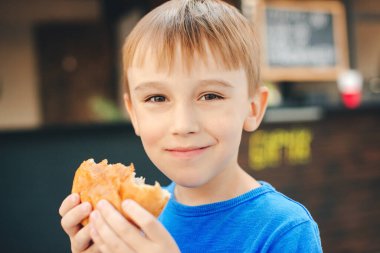 Açık kafede çörek yiyen mutlu çocuk. Ellerinde taze pişmiş çörek. Tatlı çocuk iştahlı çörek yiyor..
