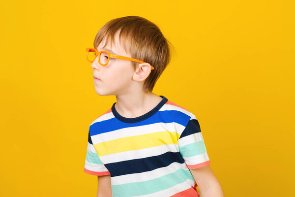 Curious boy looking aside and listens somethink. Human face expression, emotion, body language, life perception. Smart boy in glasses over yellow background.