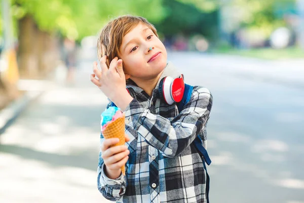 Happy boy eating ice cream outdoors. Kid walking at park in sunny day. Stylish boy outdoors. Tasty ice cream. Summer vacation. Lifestyle, fashion and vacation