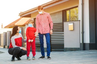 Dışarıda maske takan genç bir aile. Koronavirüsü önleme. Oğlu ve ailesi yürüyüşe çıkmış. Yeni gerçek hayat. Koronavirüsle savaş. Koronavirüs salgınını korumak için güvenlik maskesi. Karantina.