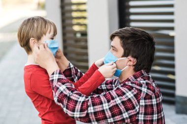 Baba, oğlu maskesini dışarıda takıyor. Coronavirus karantinası. Coronavirüs salgını, virüs belirtileri. Karantina sırasında yüz maskesi takan aile. Coronavirüs salgını.