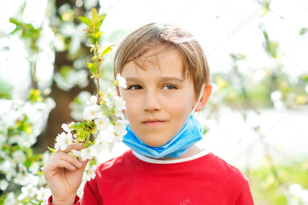 Little boy takes off a face mask. Boy breathe fresh air in a park. Spring blooming tree. No more quarantine. Breathe deep. Coronavirus ended. Quarantine is over. Health care concept.