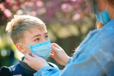 Anne oğluna dışarıda bir yüz koruyucu maske takıyor. Coronavirus, hastalık, enfeksiyon, karantina, tıbbi maske, COVID-19. Coronavirus karantinası. Yakın çekim tıbbi maske. Yüz maskesi takan çocuk.