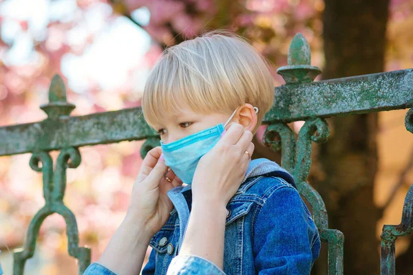 Little boy and mom in medical mask. Mother puts on her baby sterile medical mask. Child, wearing face mask, protect from infection of virus, pandemic, outbreak and epidemic of disease on quarantine.