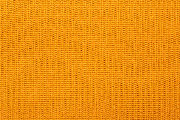 Orange knitted pattern of acrylic yarns, closeup. Yellow texture knitted wool scarf. Yellow textile background knitwear. Wool background, top view.