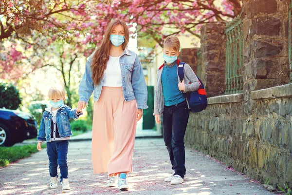 Mother and pupil of primary school go hand in hand. Sad family going home during quarantine. Family wearing face masks. Springtime. Health care concept. Back to school. Education. Real life 2020.