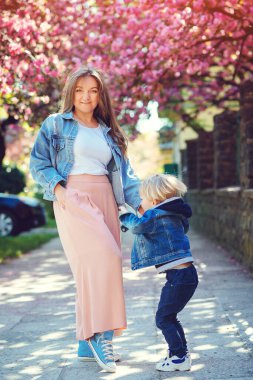 Mutlu anne ve oğul bahar caddesinde yürüyor. Şirin çocuk ve annesi dışarıda birlikte eğleniyorlar. Bahar yaşam tarzı. Anneler Günün kutlu olsun. Aile, moda ve tatiller. Neşeli çocuk ve genç anne baharın tadını çıkarın..
