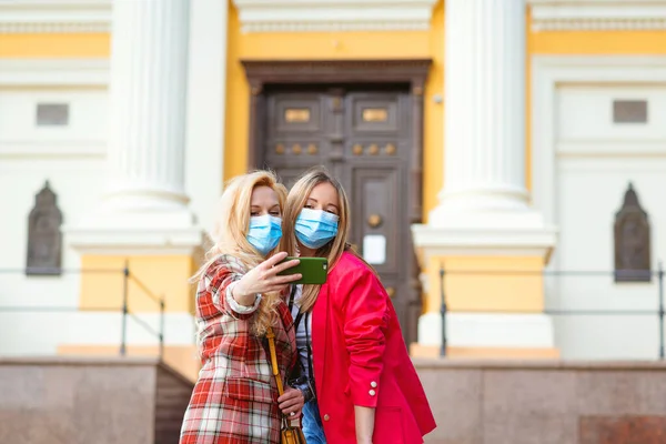 幸せな若い女の子が街で自撮り 顔のマスクを2人の女性が通りを歩いている 友達は街を一緒に旅行する コロナウイルスパンデミックの間の夏休み ヨーロッパ旅行 — ストック写真