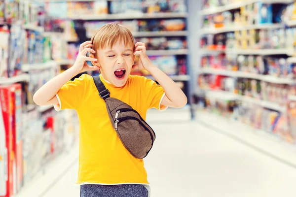 Little boy getting hysterical in toy shop. Kid makes difficult choice in supermarket. Many toys around. Boy can not selecting toy in kids store. ?hildrens tantrum in the store. Shop toys. Toy store.