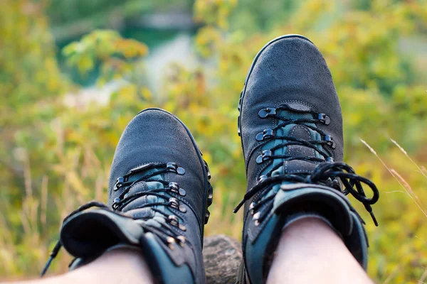 Male legs in hiking boots resting on hillside. Relaxing time during a trekking in a mountains. Beautiful view of mountains. Concept of travelling, hiking and alpinism.