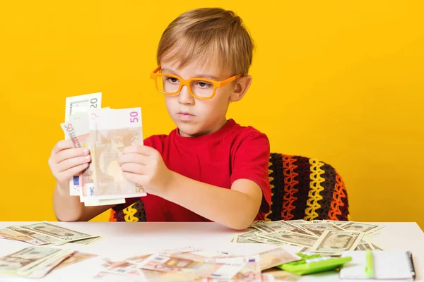 Sevimli çocuk parasını öder. Para tasarrufu konsepti. Gözlüklü küçük çocuk nereye yatırım yapacağını düşünüyor. Gelecek eğitim için para. Çocukların finansal okur yazarlığı. Finans sektörü yatırımı.