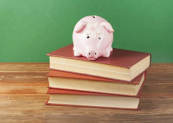 Ροζ κουμπαράς με βιβλία σε ξύλινο υπόβαθρο. Έννοια της χρηματοδότησης της εκπαίδευσης. — Φωτογραφία Αρχείου