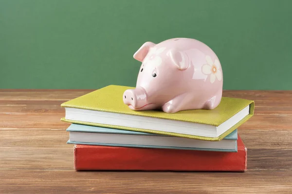 粉红色的小猪银行与书籍的木制背景。资助教育的概念 — 图库照片