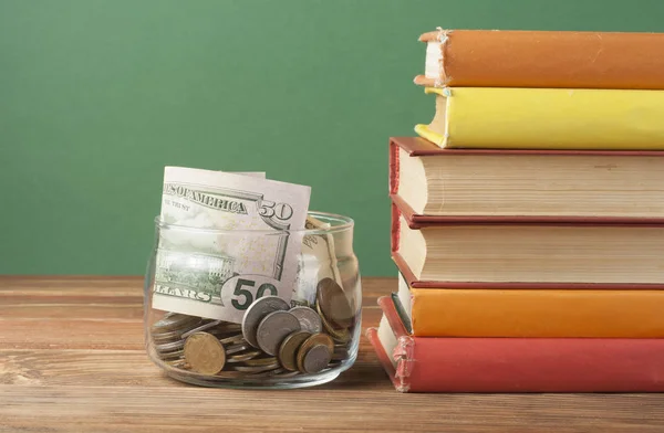 Monety w słoik i stos książek na drewnianym stole. Zapisywanie, koncepcja financiai i edukacja. — Zdjęcie stockowe