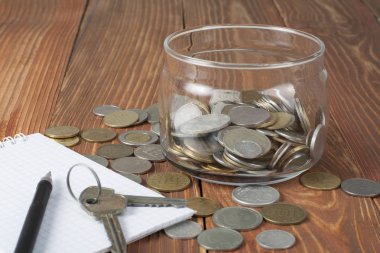 Ev tasarruf, bütçe kavramı. Not Defteri, kalem, anahtarları ve para cam ahşap Ofis Masası üzerinde.