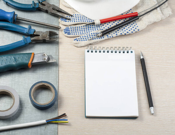 .Set of electrical tools, white helmet and notepad on metallic background. Energy concept.