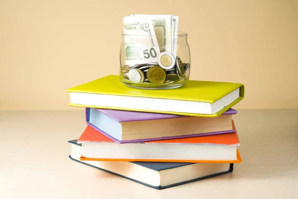 Χρήματα σε γυάλινο βάζο και στοίβα των βιβλίων πάνω ξύλινο τραπέζι. Εξοικονόμηση, έννοια financiai και εκπαίδευση. — Φωτογραφία Αρχείου