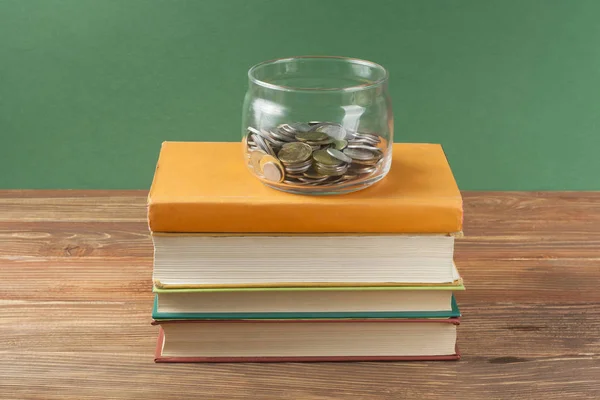Κέρματα σε γυάλινο βάζο και στοίβα των βιβλίων πάνω ξύλινο τραπέζι. Εξοικονόμηση, έννοια financiai και εκπαίδευση. — Φωτογραφία Αρχείου
